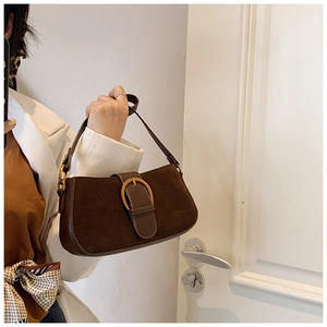 Detail of dark brown baguette bag featuring suede patchwork and gold oval buckle