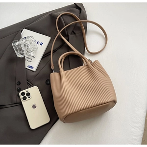 Detailed view of beige pleated bucket bag with top handle and adjustable shoulder strap