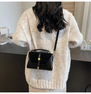Detail of a black crossbody square bag with gold metal clasp on a beige sweater