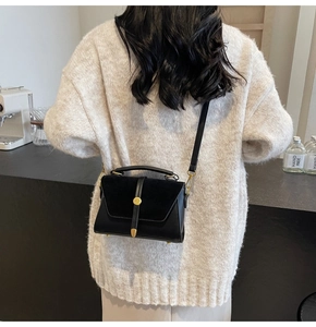 Detail of black suede and leather crossbody bag with round gold buckle and handle