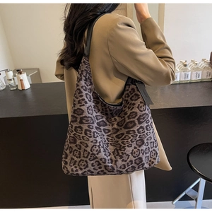 Detail of large leopard print tote bag with black leather straps on woman's shoulder