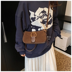 Brown suede underarm bag detail featuring a decorative gold horseshoe buckle and slim strap