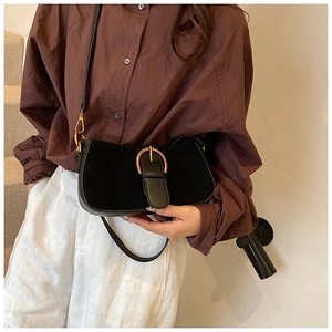 Detail of a black underarm bag featuring a large gold buckle on smooth and suede leather