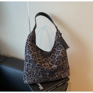Detail of grey leopard print tote bag with black leather handle on a leather sofa