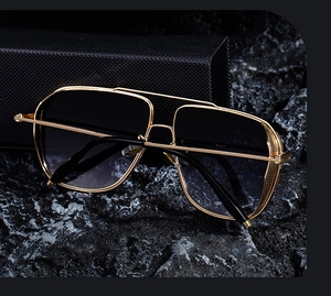 Close-up of gold metal frame sunglasses with gradient lenses on a textured rock background