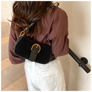 Close-up of black suede underarm bag with large gold buckle on model's shoulder