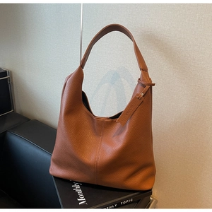 Close-up of caramel pebbled leather tote bag with vertical stitching on a black sofa