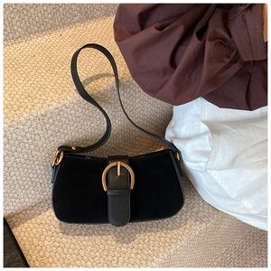 Detail of black suede underarm bag featuring a prominent gold horseshoe buckle