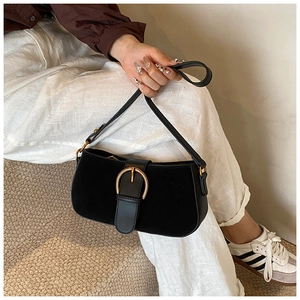 Detail of black suede shoulder bag with a large gold buckle held by a model