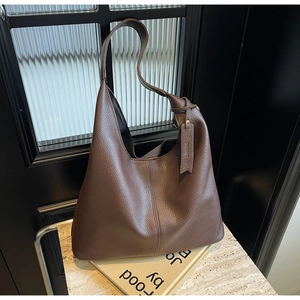 Detail of dark brown lychee grain leather tote bag with vertical stitching on stone surface