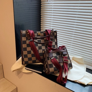 Brown checkerboard tote bag set with wide red shoulder strap in a retro indoor setting