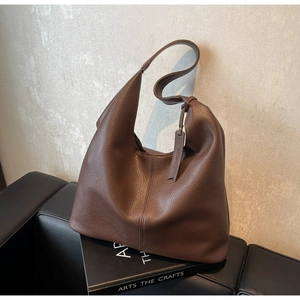Close-up of a large dark brown leather tote bag with pebble grain texture on a leather chair
