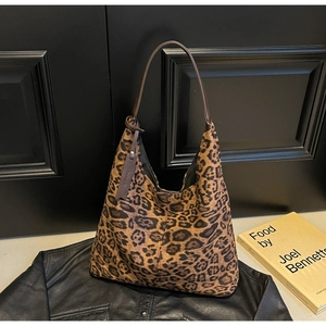 Close-up of leopard print hobo tote bag with brown leather strap on a black leather jacket