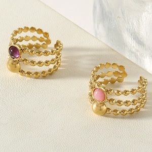 Detail of layered gold beaded rings with round purple and pink stones on a white stand