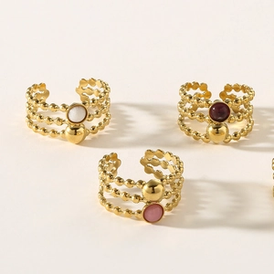 Three-layer gold beaded titanium steel rings with assorted natural stones on beige surface