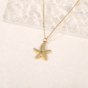 Detail of a 18k gold starfish pendant with fine textured surface on a beige background