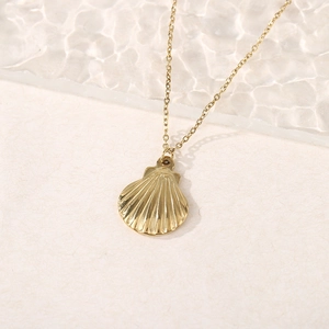 Detailed shot of a gold scallop shell pendant necklace on a rippled glass surface