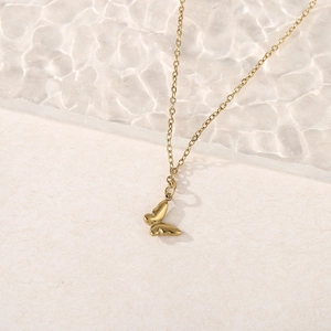 Detail of 18k gold butterfly pendant necklace on a textured ripple glass background