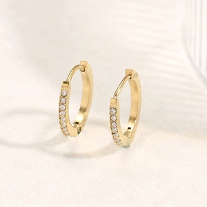 Vue macro de boucles d'oreilles huggie en or 18 carats avec zircons et acier poli