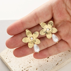 Detailed view of gold flower earrings with small central pearl and large teardrop pearl drop