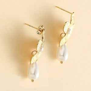 Macro detail of gold flower earrings featuring brushed metal texture and pearl pendants