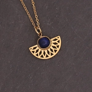 Detailed shot of a gold geometric fan pendant with blue lapis stone on gray rock