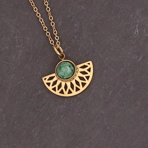 Macro shot of fan-shaped gold pendant with green stone on dark stone surface