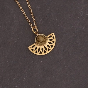 Detail of fan-shaped gold titanium steel pendant with brown natural stone on stone surface