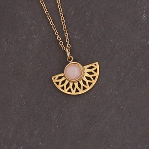 Detailed macro view of a gold fan-shaped necklace with a pink gemstone on a stone surface