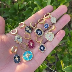 Detail of 18K gold-plated star and coin pendant earrings set held in hand outdoors