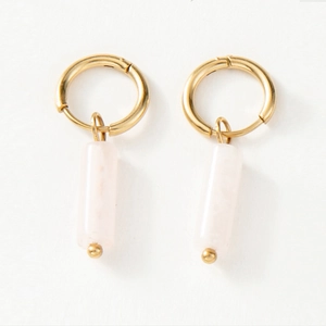 Détail de boucles d'oreilles créoles dorées avec pendentifs cylindriques en pierre rose