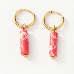 Détail de créoles dorées avec pendentifs cylindriques en pierre marbrée rose et blanc