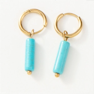 Détail de boucles d'oreilles créoles dorées avec pendentifs cylindriques en turquoise