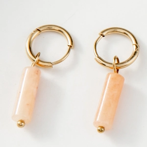Détail de créoles dorées avec pendentifs cylindriques en pierre naturelle rose poli
