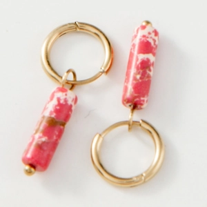 Détail de boucles d'oreilles créoles dorées avec pendentifs en pierre marbrée magenta