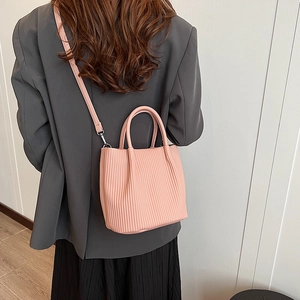 Pink pleated bucket bag with round handle and shoulder strap shown with a modern outfit