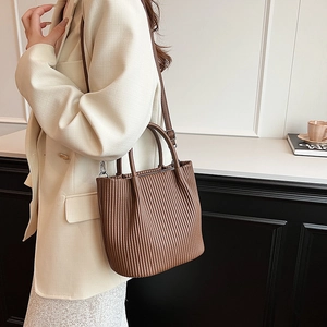 Deep brown pleated bucket bag with dual handles and slim shoulder strap shown on model