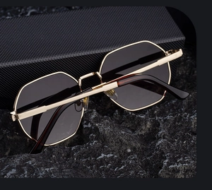 Detail view of square gold metal sunglasses featuring dark lenses on a premium black case