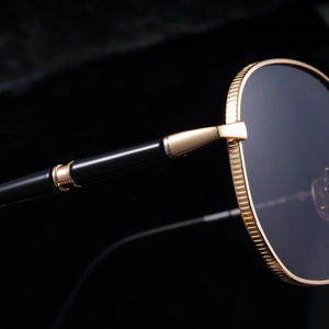 Macro shot of gold metal frame with coin texture and black temples for square sunglasses