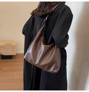 Detail view of large brown vintage leather hobo bag worn over a black coat for women