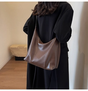 Detail of a large dark brown hobo bag with a polished oily finish worn by a model