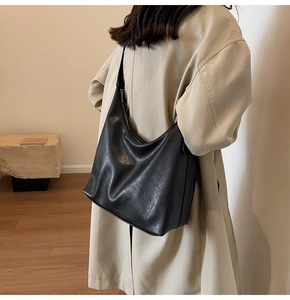 Close-up of a black oversized faux leather tote bag worn by a model in a minimalist setting
