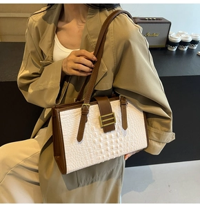 Detail of white crocodile textured leather tote bag with brown straps and gold metal buckles