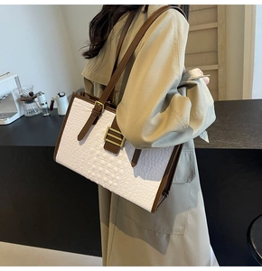 Detail of white crocodile-embossed tote bag with brown straps worn by a model in a cafe