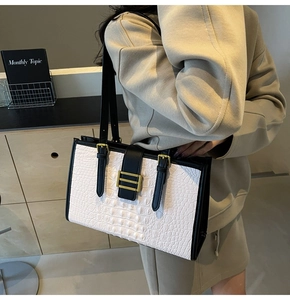 Detail of white crocodile pattern tote bag with black strap and vintage golden buckle