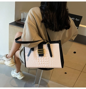 Detailed view of crocodile embossed white tote bag with black trim and gold buckle