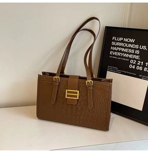Detail of crocodile embossed brown tote bag featuring a golden H-shaped metal buckle