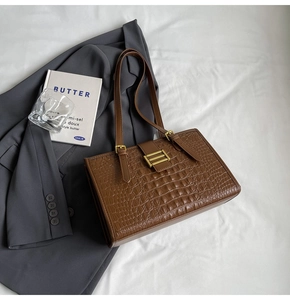 Detail of dark brown crocodile embossed tote bag with gold metal buckles and matte leather
