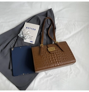 Brown crocodile leather tote bag with gold buckle detail shown with tablet and books