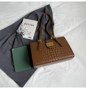 Close-up of brown crocodile texture tote bag with golden buckle on a stylish desk